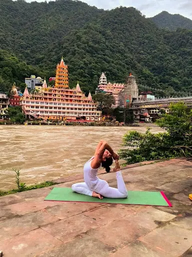 Laura nella posizione del piccione sul tappetino, davanti al fiume e ai templi di Rishikesh