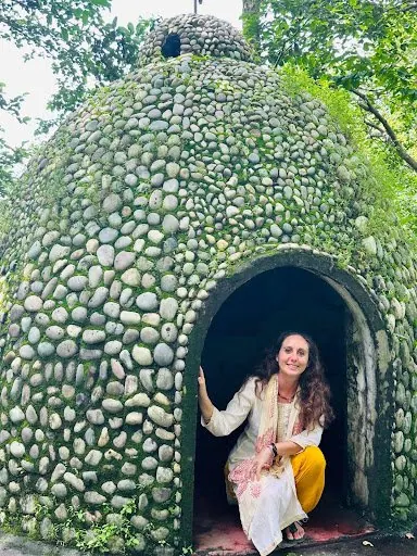 Laura sorridente all'ingresso di una piccola cella di meditazione in pietre ricoperte di muschio, in India