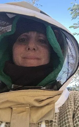 Laura con la maschera da apicoltrice, fra i rami di un olivo sotto il cielo azzurro
