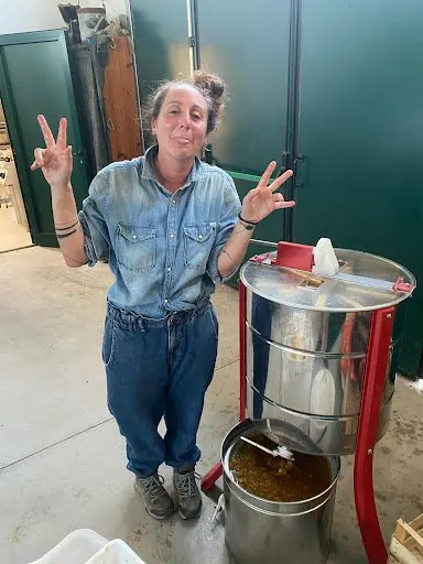 Laura sorridente accanto allo smielatore, con il miele appena estratto nel secchio