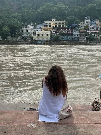 Laura seduta di spalle sui gradini del ghat, davanti al Gange e alle case di Rishikesh