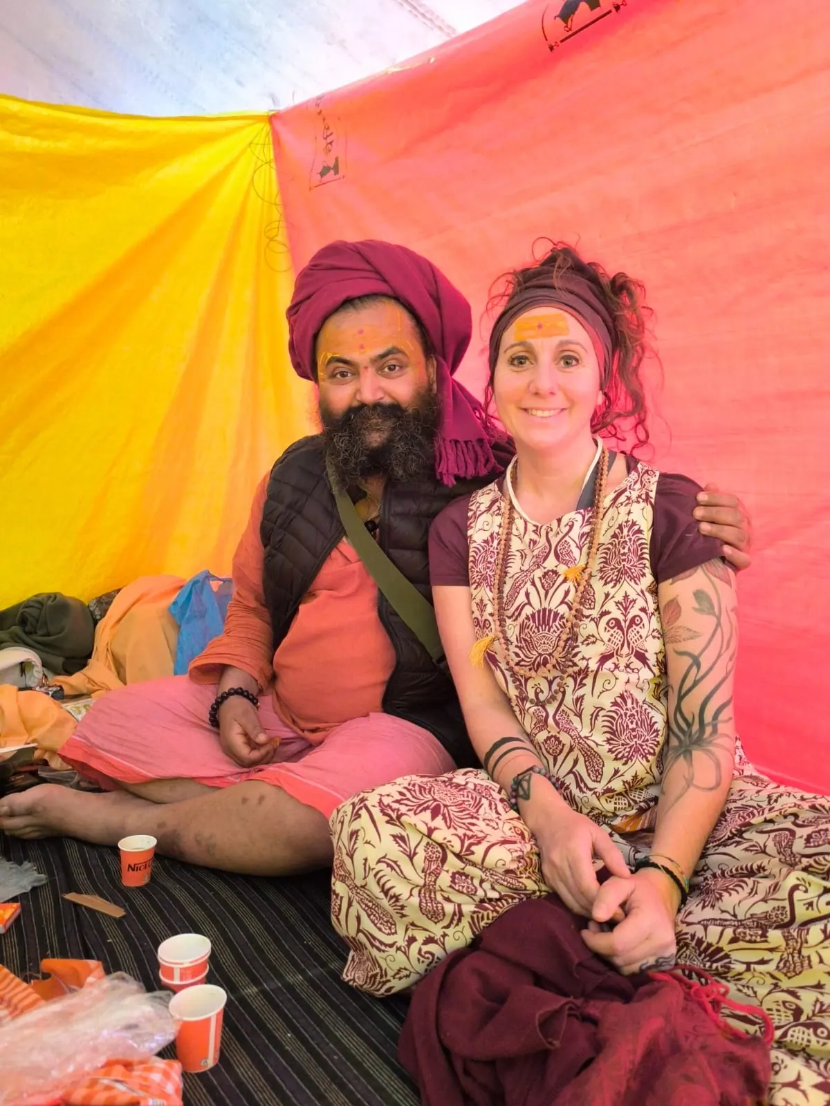 Laura Buoncristiani seduta accanto a un sadhu sotto una tenda arancione al Kumbh Mela