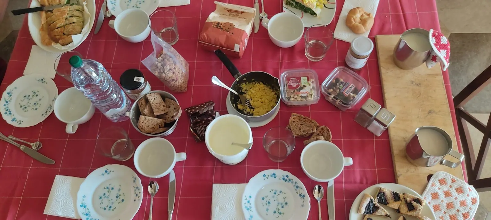 La colazione condivisa sulla tovaglia rossa, con tazze, frutta e dolci