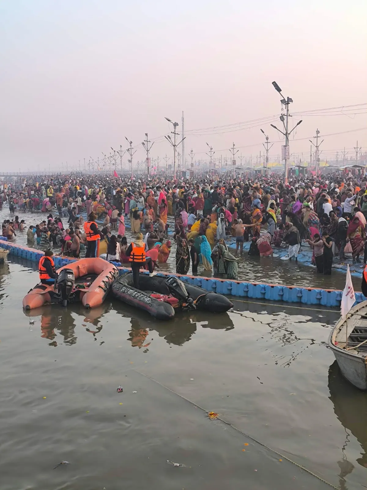 Una folla di pellegrini in riva al fiume e nell'acqua, con le barche di soccorso, al Kumbh Mela