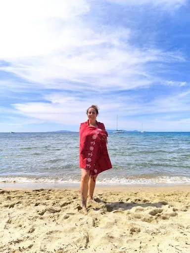 Una donna avvolta in uno scialle rosso sulla spiaggia, davanti al mare