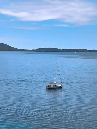 Una barca a vela nel mare calmo, con le colline sullo sfondo