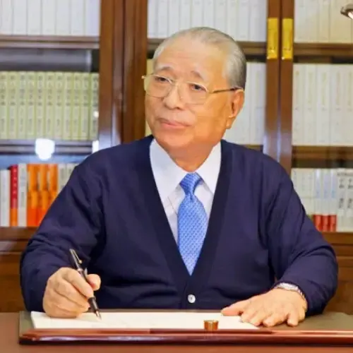 Daisaku Ikeda seduto alla scrivania con una penna in mano, davanti a una libreria