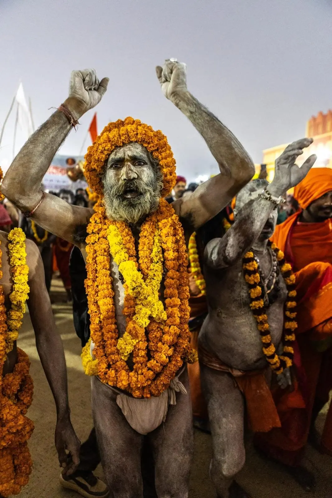 Un sadhu cosparso di cenere, con ghirlande di fiori arancioni al collo, alza le braccia al Kumbh Mela