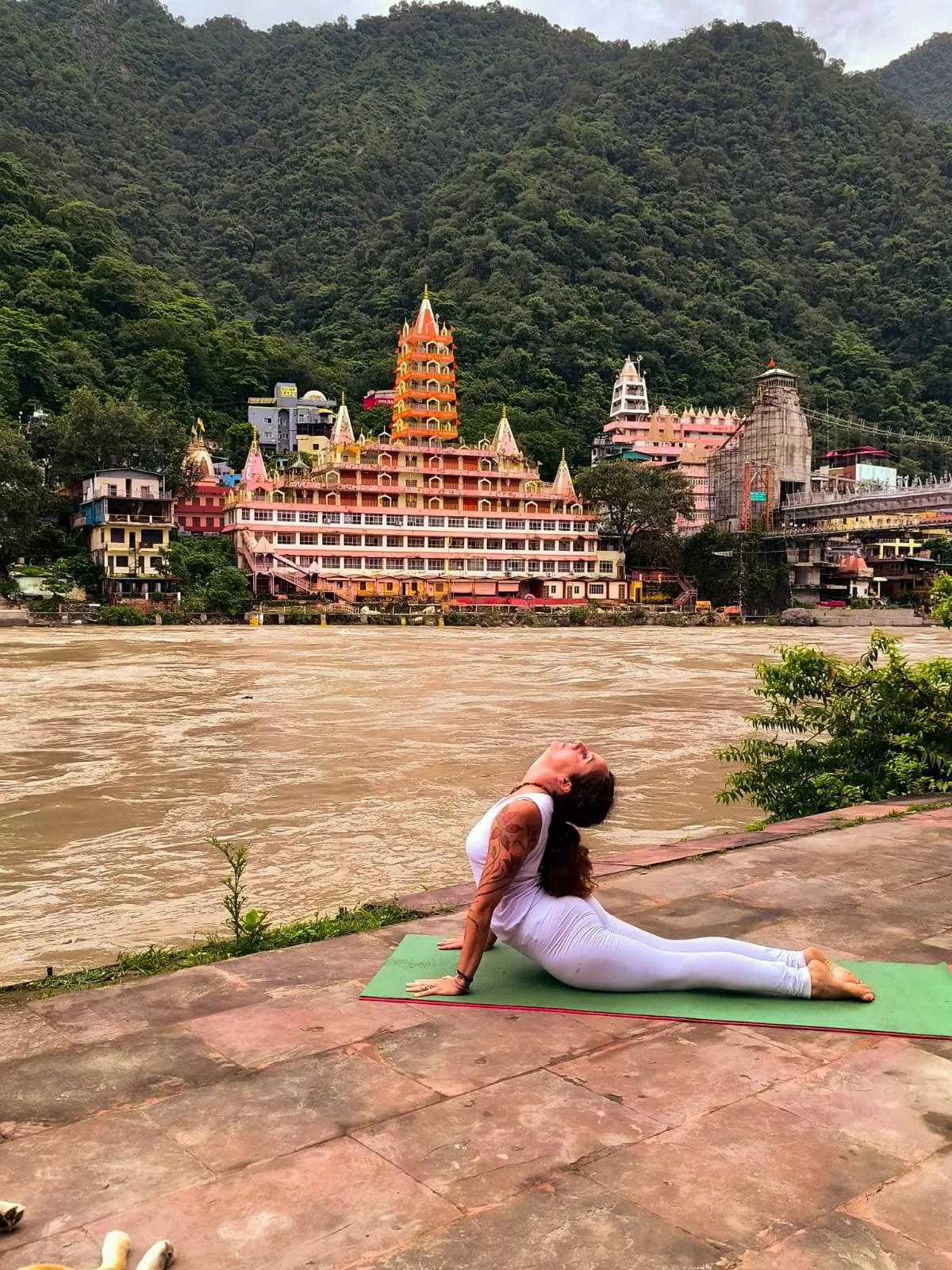 Laura nella posizione del cobra sul tappetino verde, sulla riva del Gange a Rishikesh