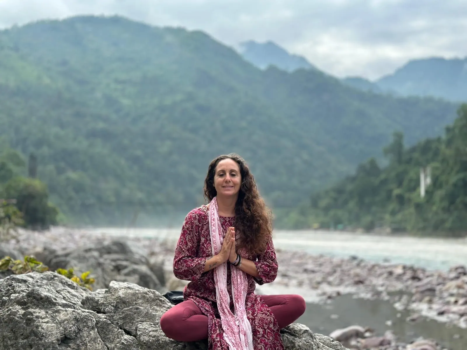 Laura Buoncristiani in meditazione sulle rocce del fiume, fra le montagne verdi