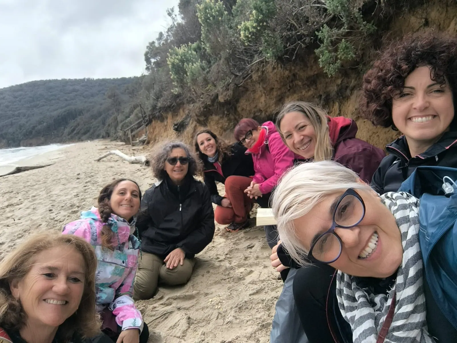 Un selfie del gruppo sorridente seduto sulla sabbia della spiaggia