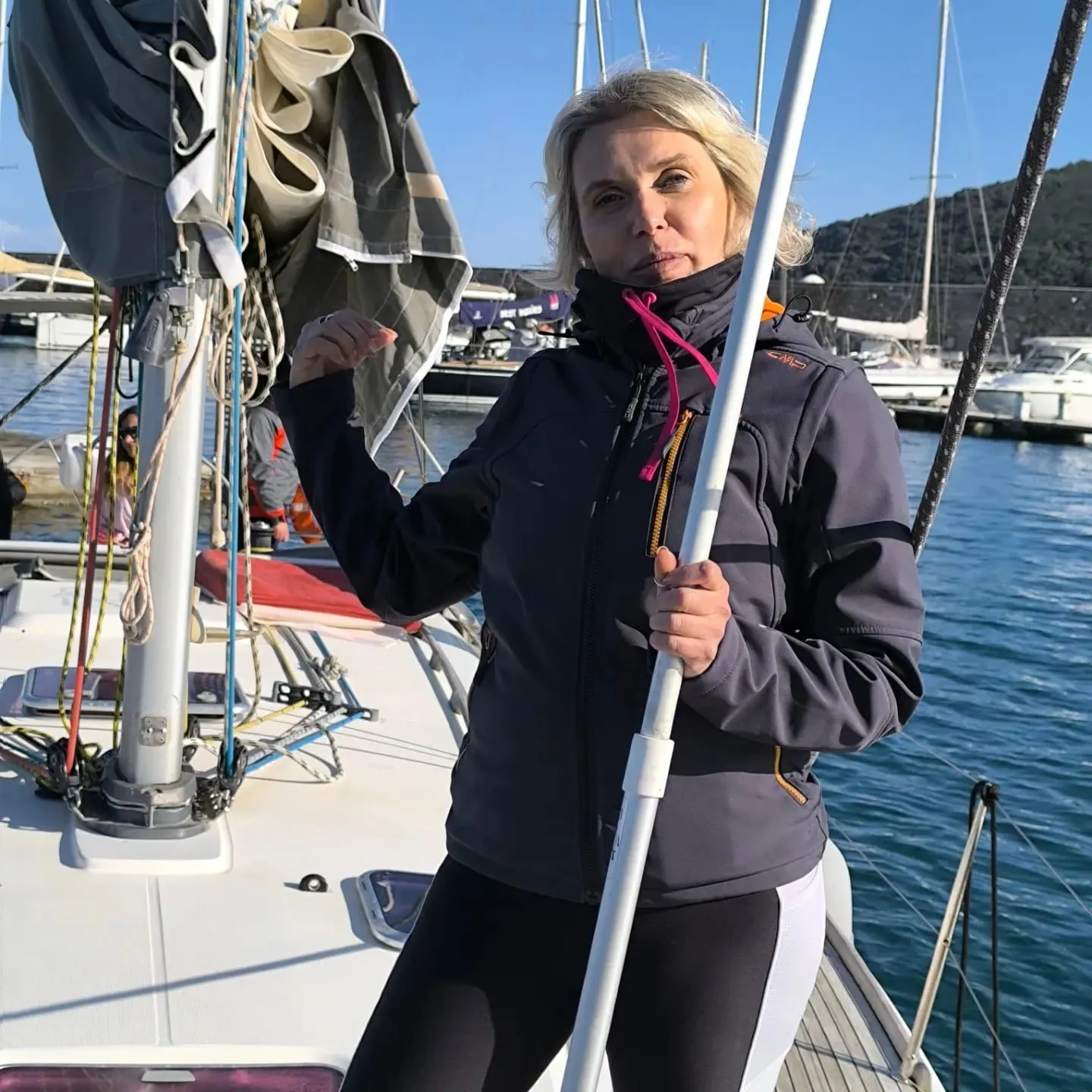 Una partecipante a bordo della barca a vela ormeggiata, con una mano sull'albero e il porto alle spalle