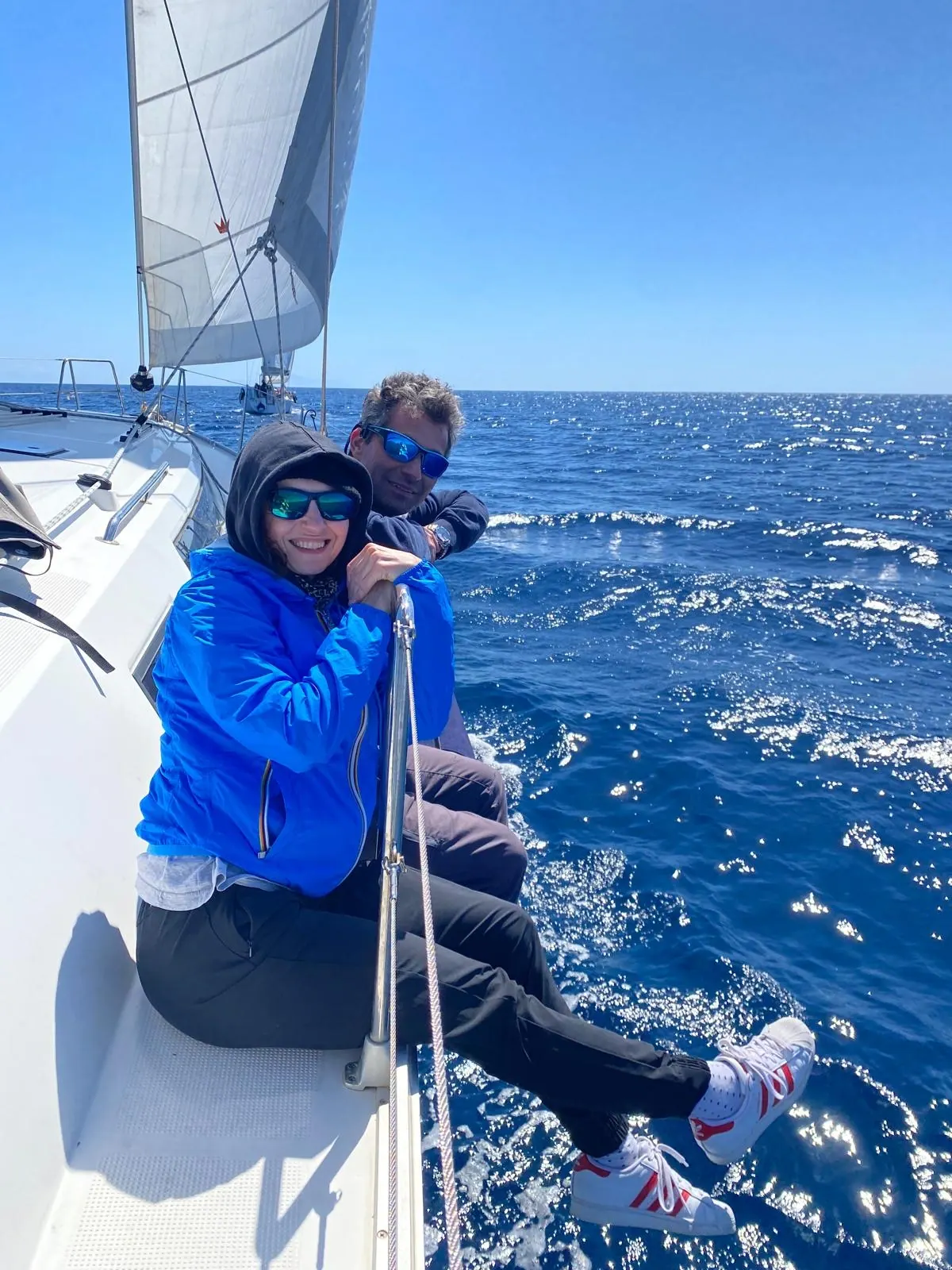 Una partecipante seduta sul bordo della barca a vela, con la vela spiegata e il mare blu intorno
