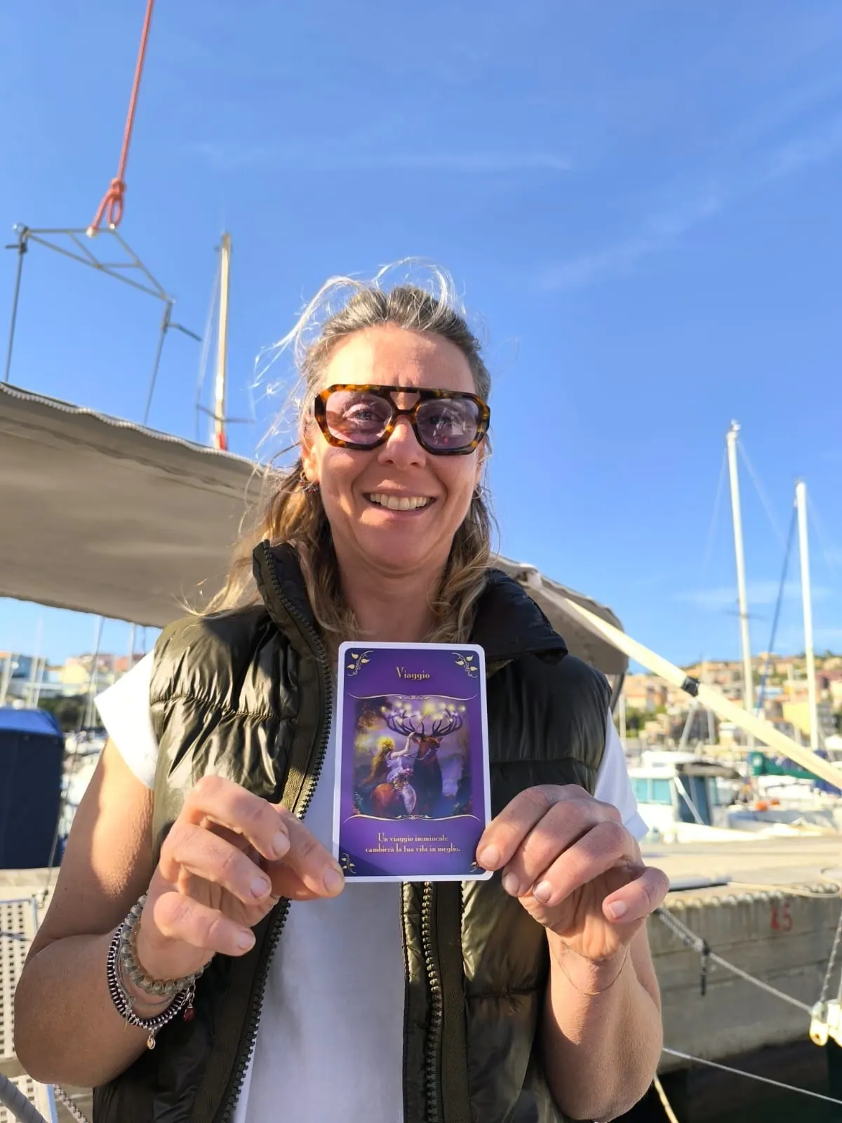 Una partecipante sorridente mostra la carta che ha pescato, sulla barca in porto