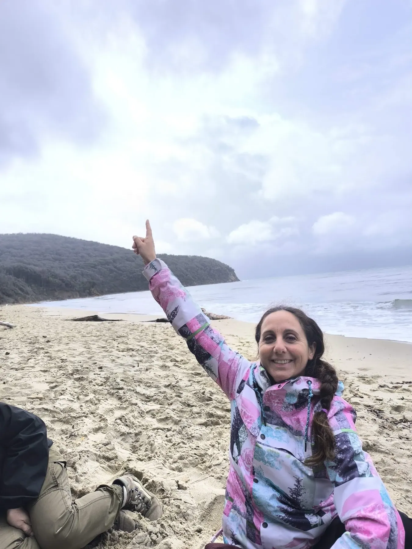 Una camminatrice sulla spiaggia di Cala Violina indica il mare, con il promontorio alle spalle