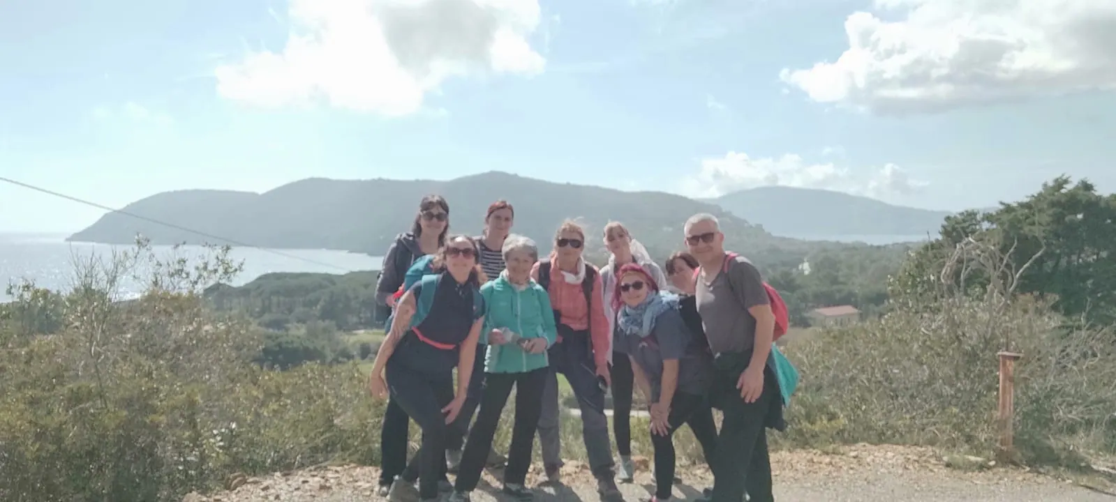 Il gruppo sorridente su un poggio, con il mare e le colline dell'isola alle spalle