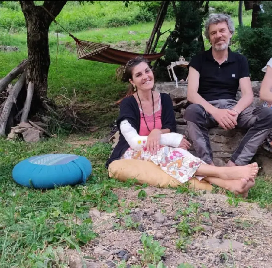 Una donna e un uomo seduti sull'erba sotto gli alberi, accanto a un'amaca