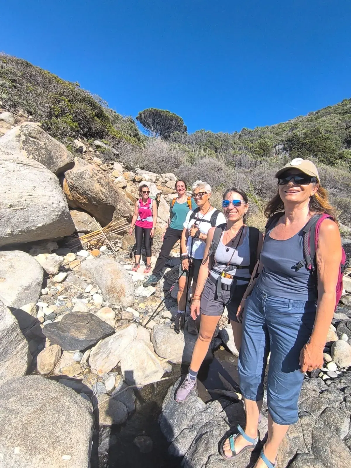 Le partecipanti in cammino su un sentiero di rocce e macchia, sotto il cielo azzurro