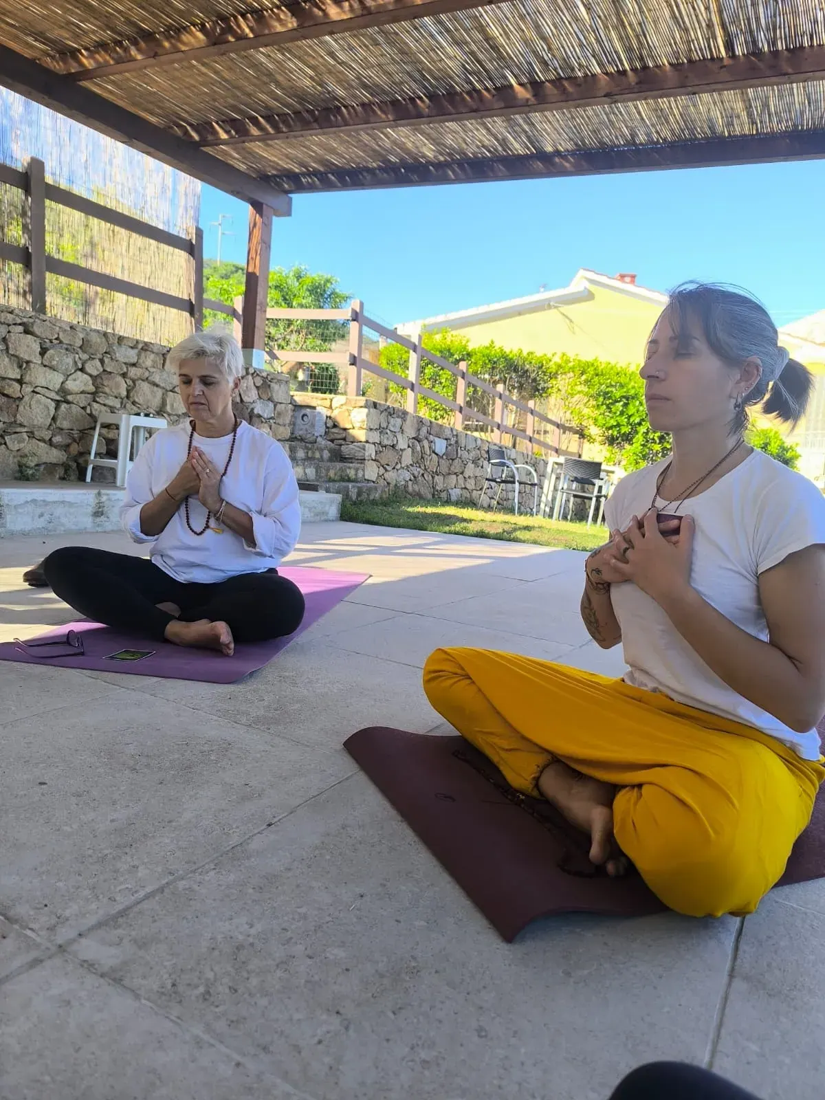 Due partecipanti in meditazione a gambe incrociate, con le mani giunte al petto