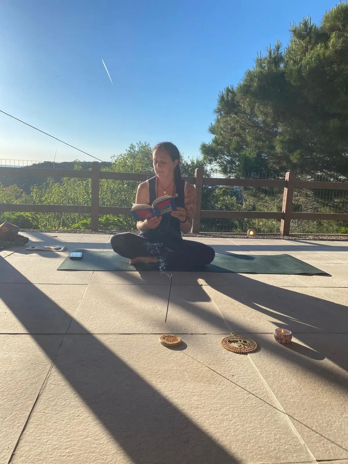 Una partecipante in meditazione sul tappetino della terrazza, fra il sole e le ombre dei pini