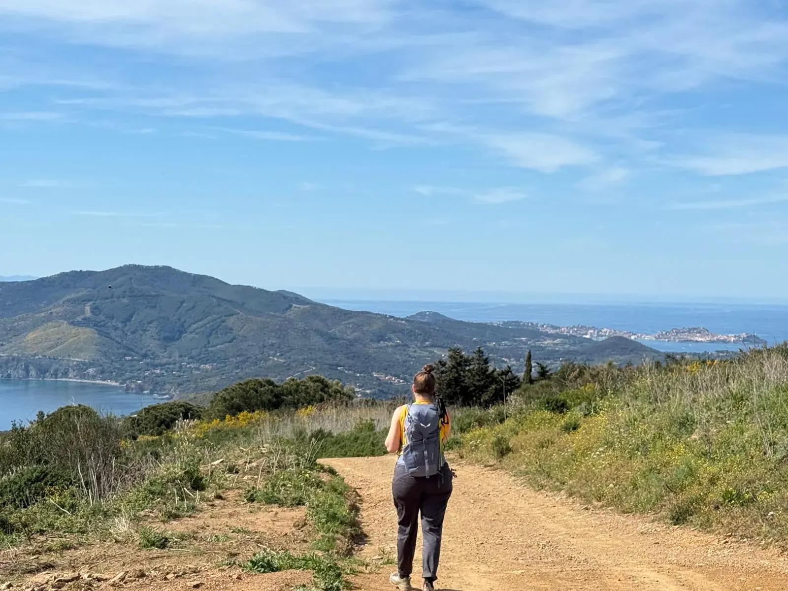 Una camminatrice su un sentiero di crinale, con le colline e il mare dell'Elba davanti