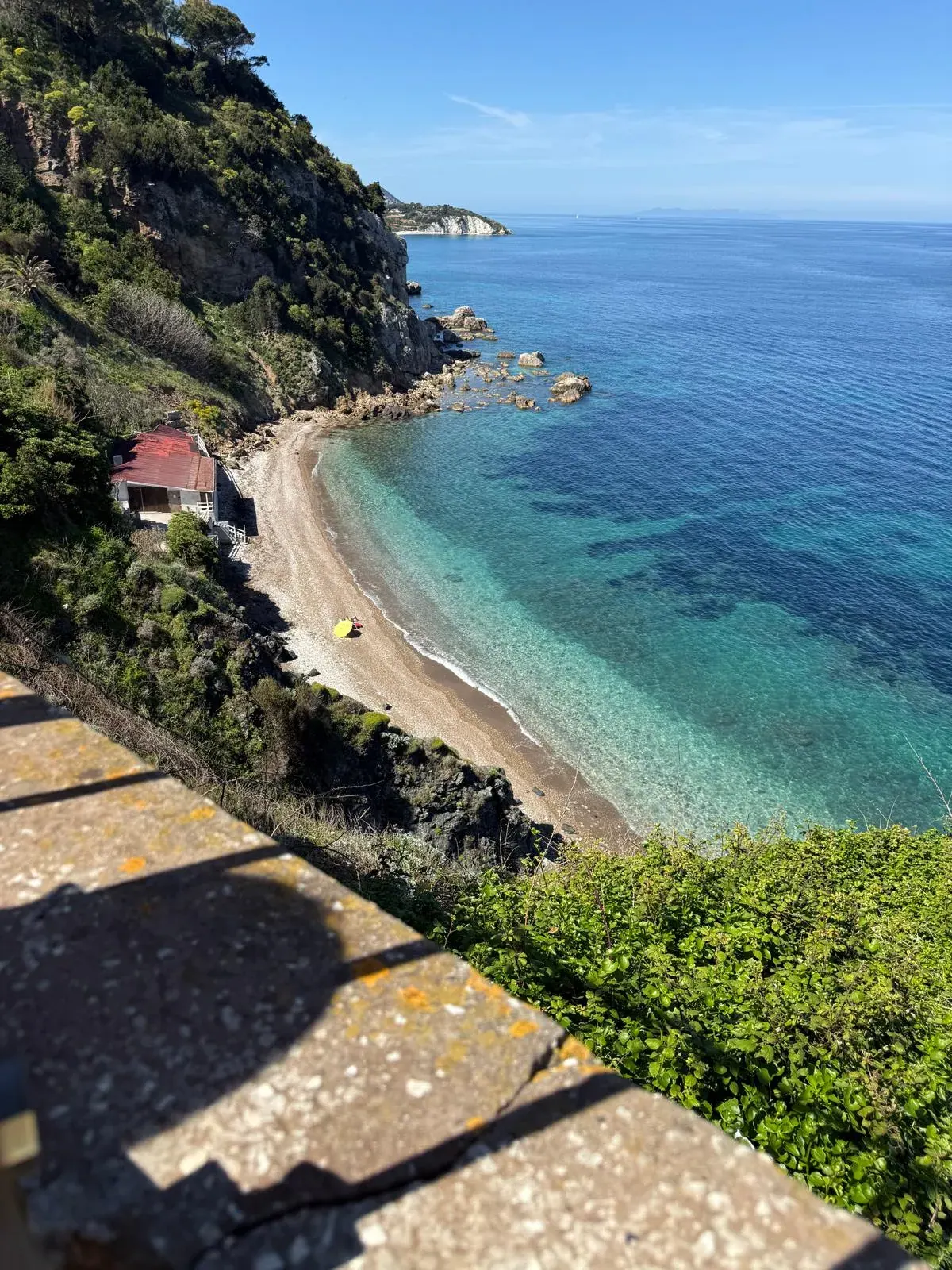 Una lunga spiaggia chiara e il mare turchese visti dall'alto, fra le rocce e la macchia