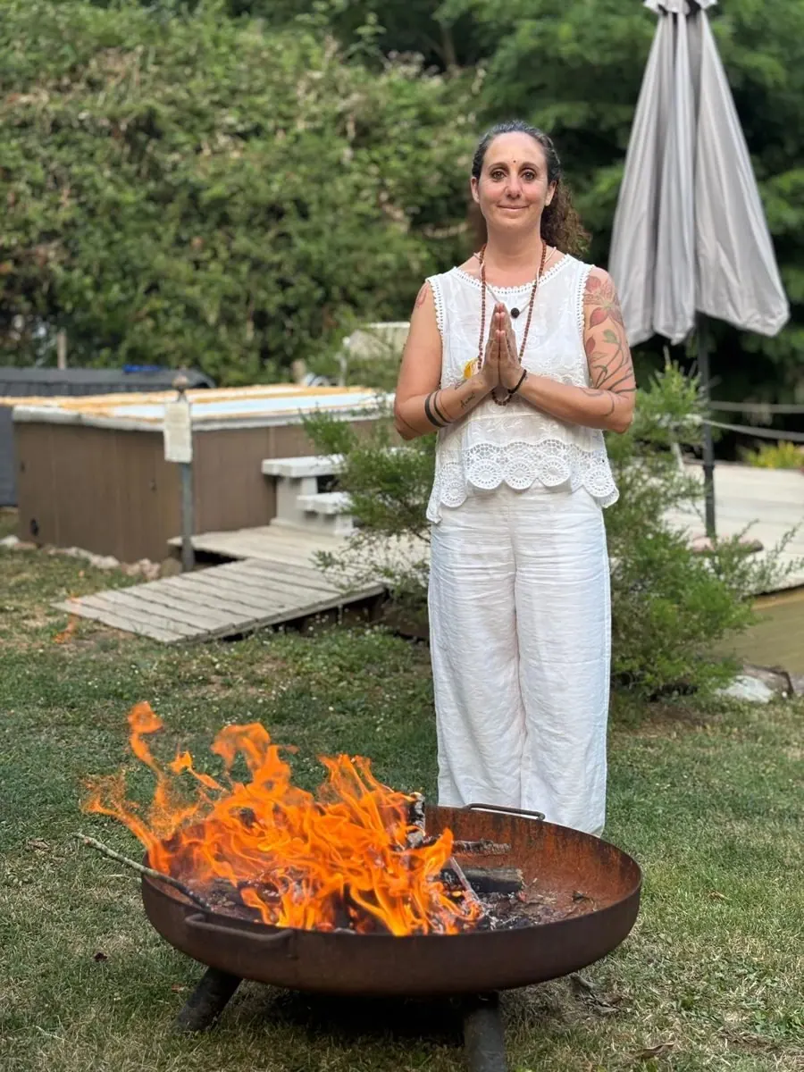 Laura Buoncristiani vestita di bianco, a mani giunte davanti a un fuoco acceso in giardino